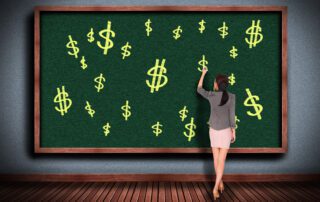 teacher writing dollar signs on chalkboard to show cash in the classroom