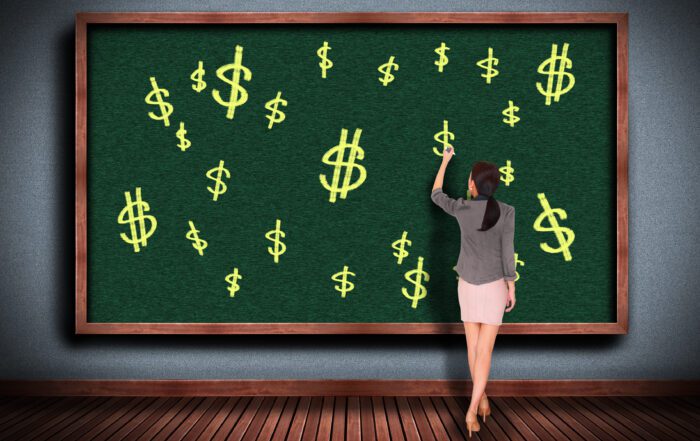 teacher writing dollar signs on chalkboard to show cash in the classroom
